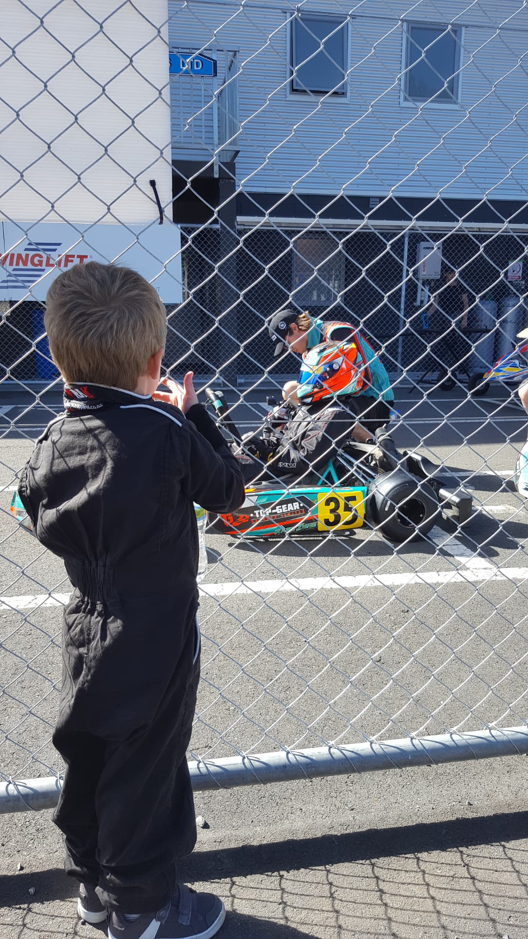 Young Niko in racing overalls watching from behind the pit fence